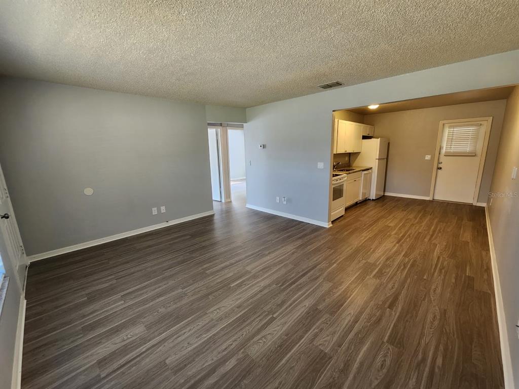 An open-concept living area with wood-look flooring leads into a kitchen with white appliances — 9530 LYNN LANE UNIT B, SEMINOLE, FL