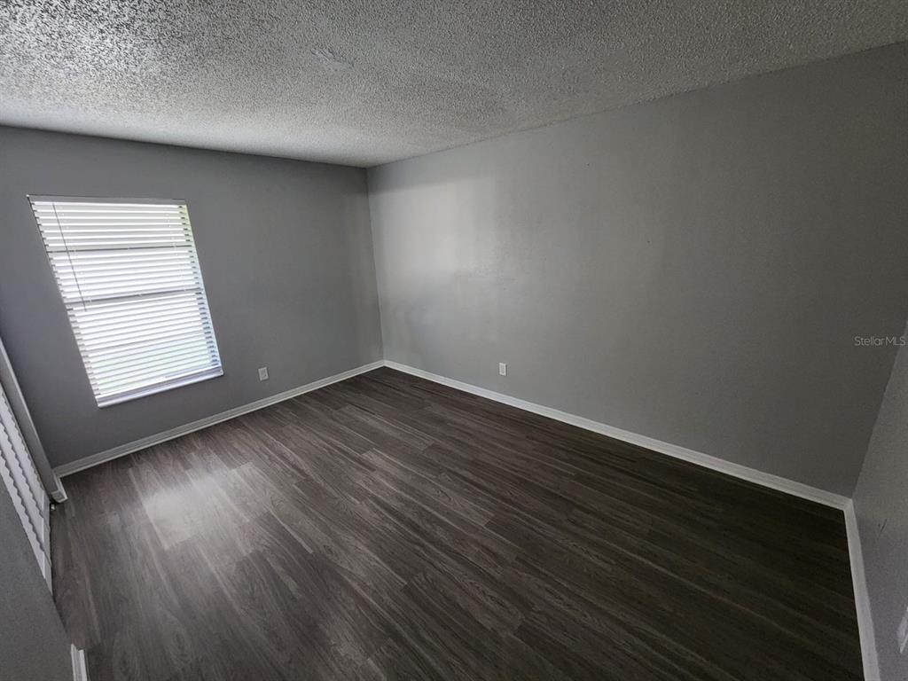 An empty bedroom features gray walls, dark wood-look flooring, and a single window with blinds — 9530 LYNN LANE UNIT B, SEMINOLE, FL