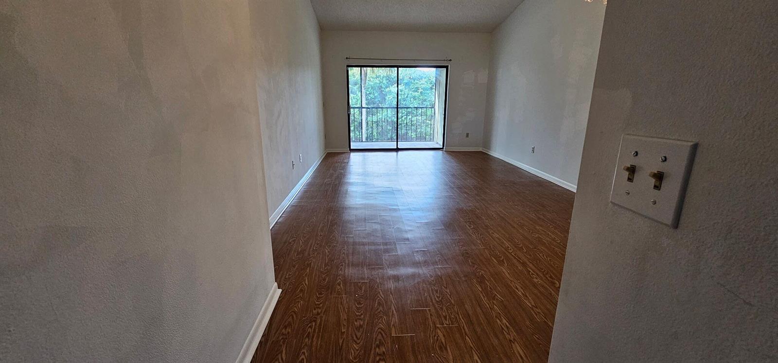An empty room with wood-look flooring, light-colored walls, and a sliding glass door to a balcony — 7879 Willow Spring Drive # 923, Lake Worth FL 33467, LAKE WORTH, FL