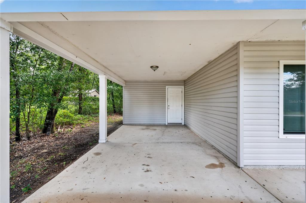A covered concrete carport features light gray vinyl siding and a single white entry door — 6255 SE 165TH COURT, OCKLAWAHA, FL