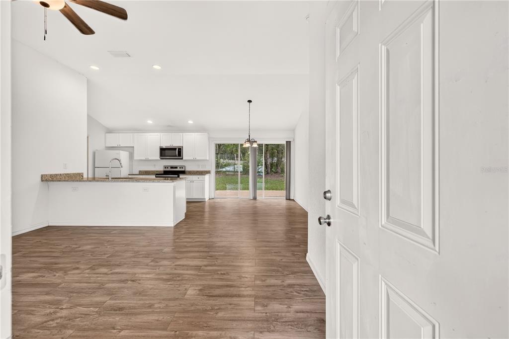 A view from a doorway into an open-concept kitchen and dining area with wood flooring — 6255 SE 165TH COURT, OCKLAWAHA, FL