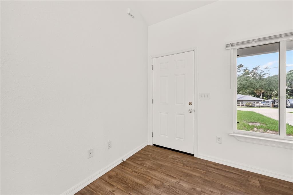 An interior view of a room with white walls, wood-look flooring, and a front door — 6255 SE 165TH COURT, OCKLAWAHA, FL