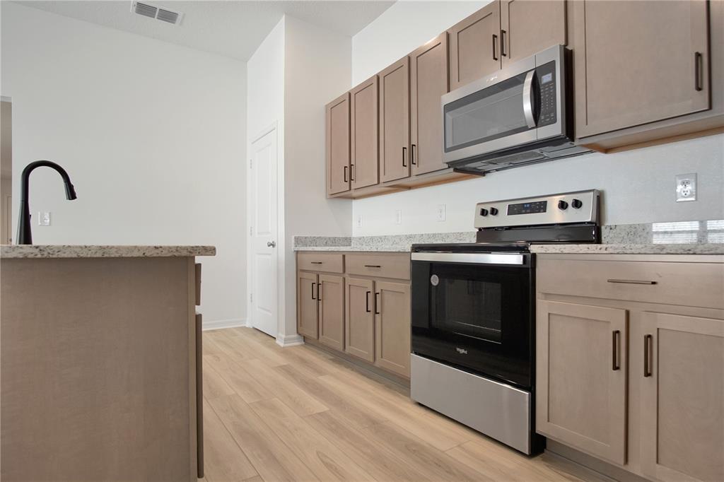 A kitchen features light wood cabinets, granite countertops, stainless steel appliances, and light wood flooring — 9224 WESTSIDE HILLS DRIVE, DAVENPORT, FL
