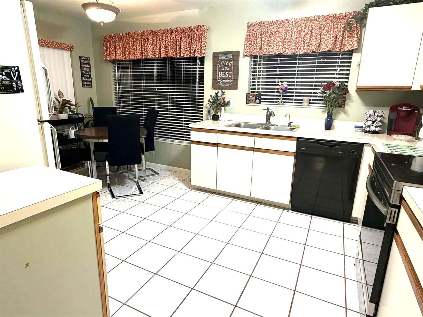 A kitchen features white cabinets, a black dishwasher, tile flooring, and a dining area — 3209 Perimeter Drive # 2713, FL 33467, FL