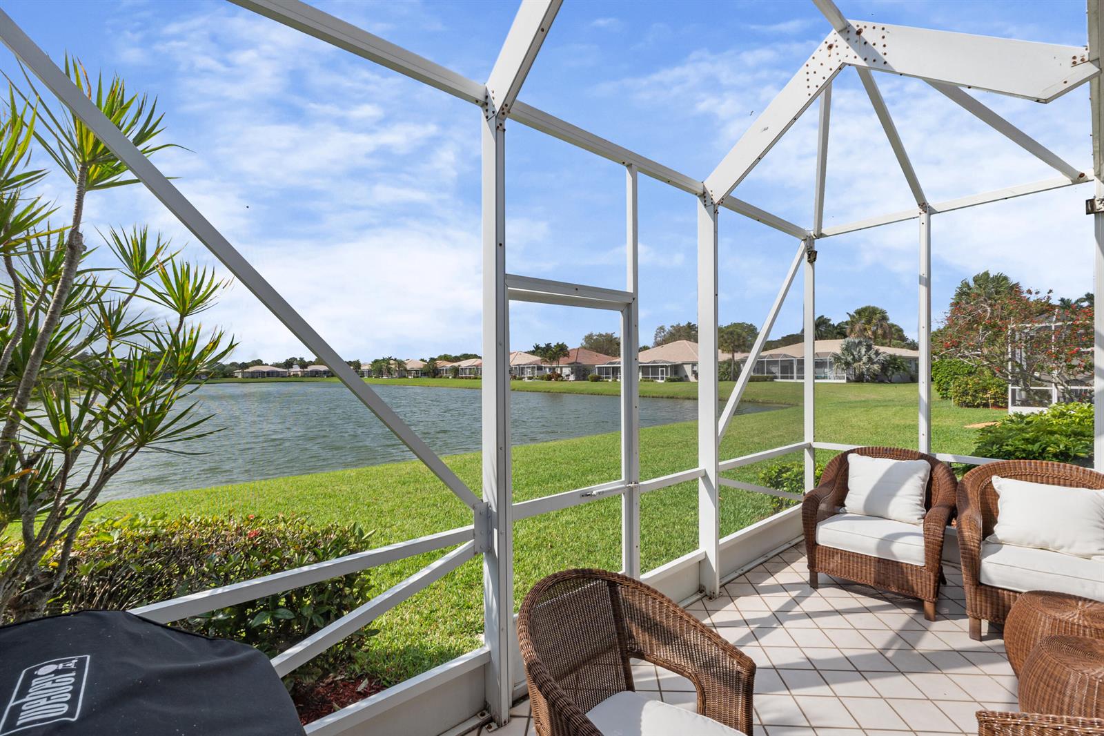 A screened-in patio with wicker furniture overlooks a grassy lawn and a lake — 10665 Royal Caribbean Circle, Boynton Beach FL 33437, BOYNTON BEACH, FL