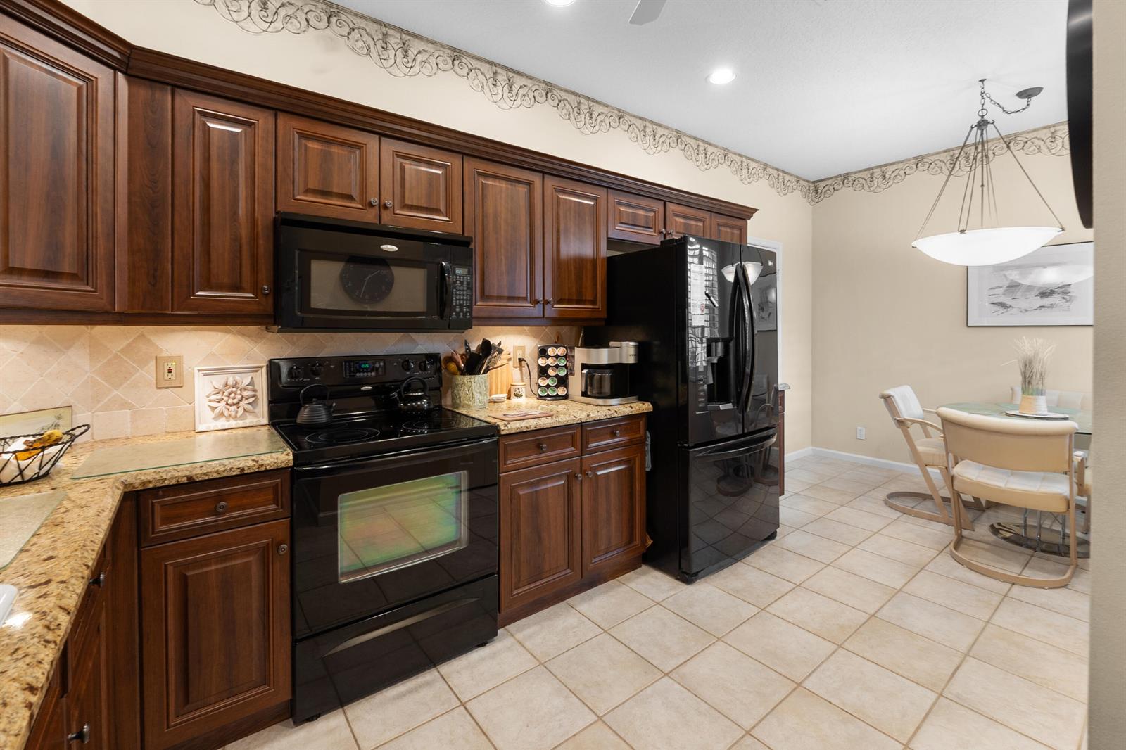 A kitchen features dark wood cabinets, black appliances, granite countertops, and a dining area — 10665 Royal Caribbean Circle, Boynton Beach FL 33437, BOYNTON BEACH, FL