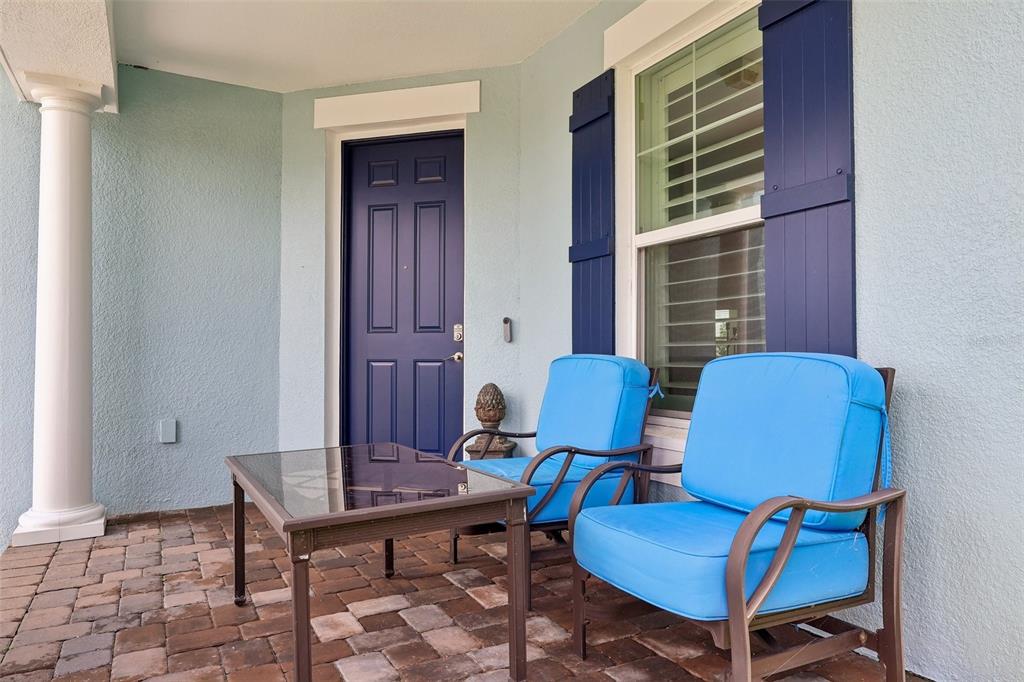 A covered patio features brick pavers, two blue chairs, a glass table, and a blue door — 343 BLUE CYPRESS DRIVE, GROVELAND, FL