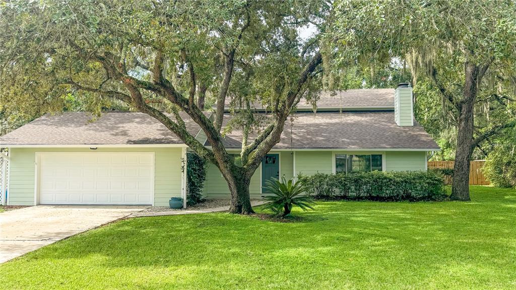 A light green single-story house with a two-car garage and large oak trees in front — 2261 CHARLOTTE DRIVE, LONGWOOD, FL