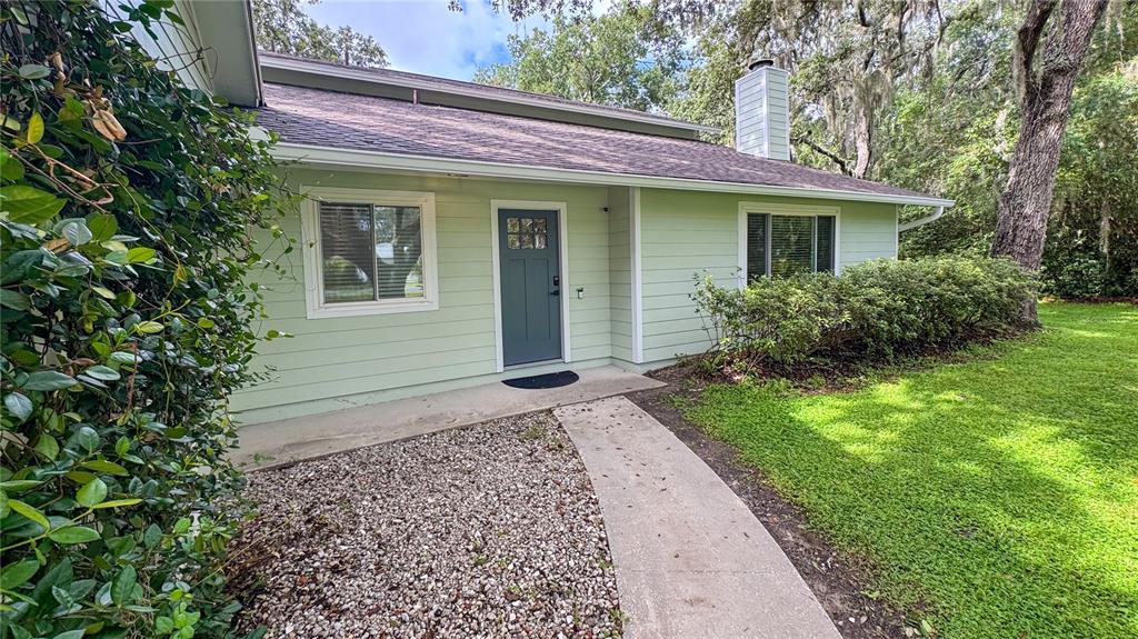 A light green house exterior features a gray front door, gravel yard, and concrete walkway — 2261 CHARLOTTE DRIVE, LONGWOOD, FL