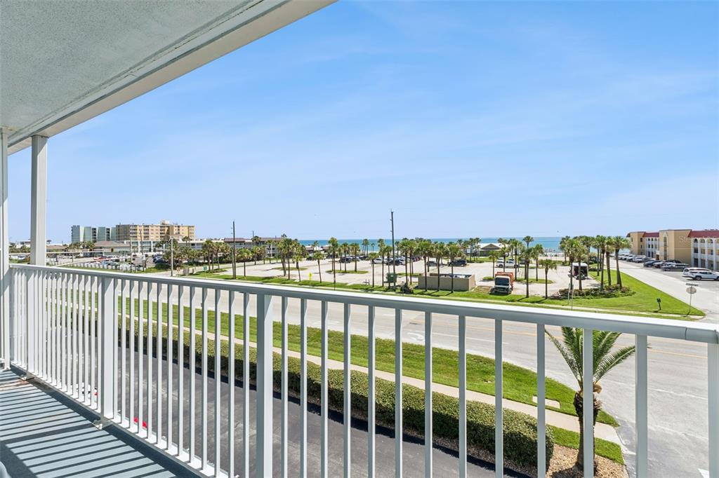 A balcony with a white railing overlooks a parking lot, palm trees, and the ocean — 3700 S ATLANTIC AVENUE UNIT 416, NEW SMYRNA BEACH, FL