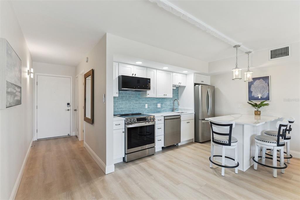 A kitchen features white cabinets, stainless steel appliances, a blue tile backsplash, and a dining island — 3700 S ATLANTIC AVENUE UNIT 416, NEW SMYRNA BEACH, FL