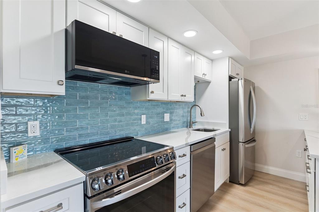 A kitchen with white cabinets, stainless steel appliances, and a blue glass tile backsplash — 3700 S ATLANTIC AVENUE UNIT 416, NEW SMYRNA BEACH, FL