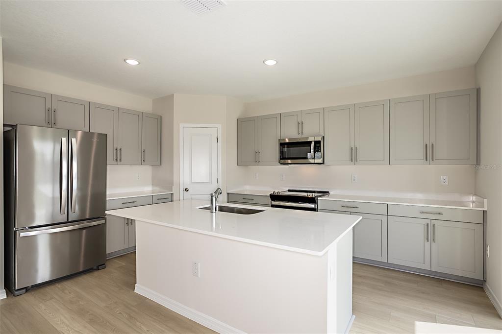 A modern kitchen features gray cabinets, stainless steel appliances, and a white quartz island countertop — 33840 NOBLE CREEK PLACE, DADE CITY, FL