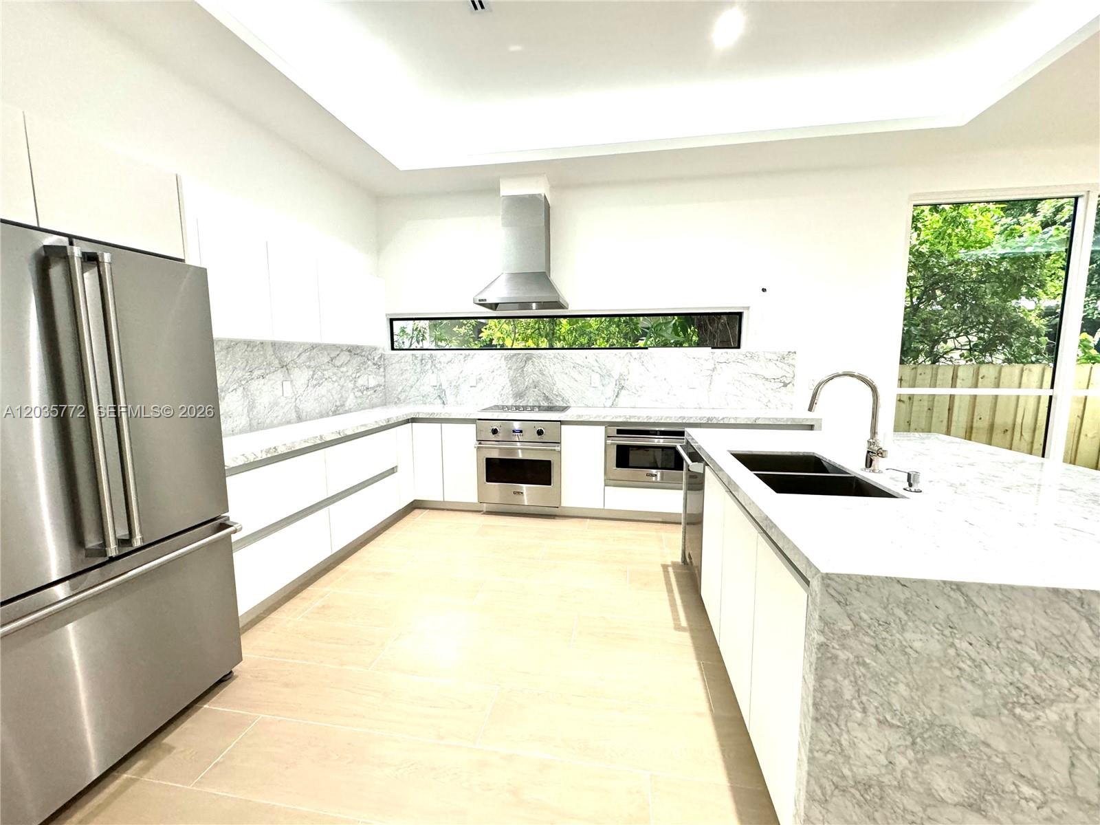 A modern kitchen features white cabinetry, marble countertops, stainless steel appliances, and a horizontal window — 5728 NW 5th Ct # 2, Miami FL 33127, MIAMI, FL