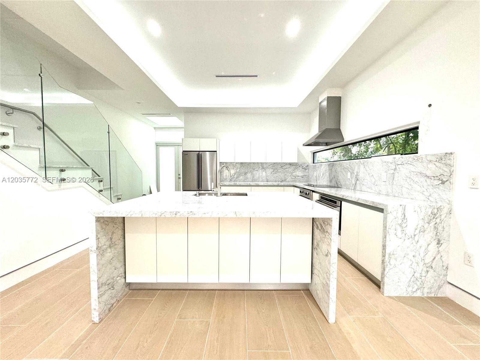 A modern kitchen features a marble waterfall island, white cabinetry, and a glass staircase — 5728 NW 5th Ct # 2, Miami FL 33127, MIAMI, FL