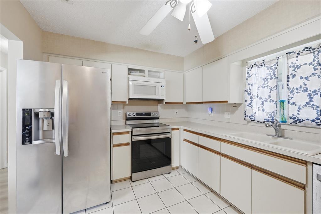 A kitchen featuring white cabinets, stainless steel appliances, a white sink, and tiled flooring — 17814 SE 107TH TERRACE, SUMMERFIELD, FL