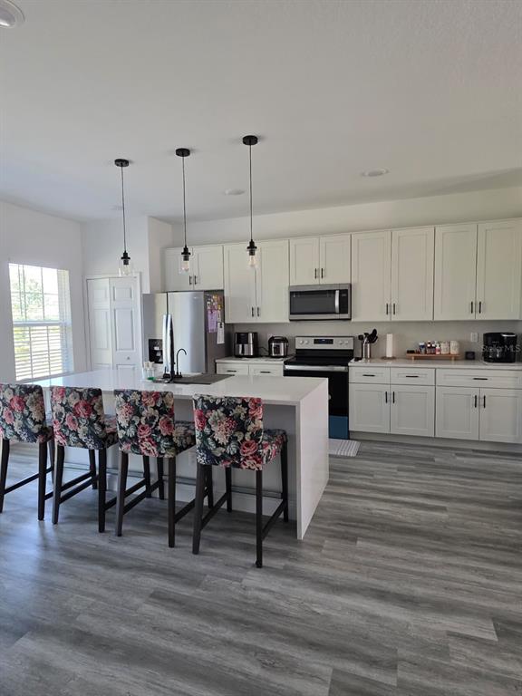 A modern kitchen features white cabinetry, a large island with floral barstools, and gray flooring — 14886 SW 43RD COURT, OCALA, FL