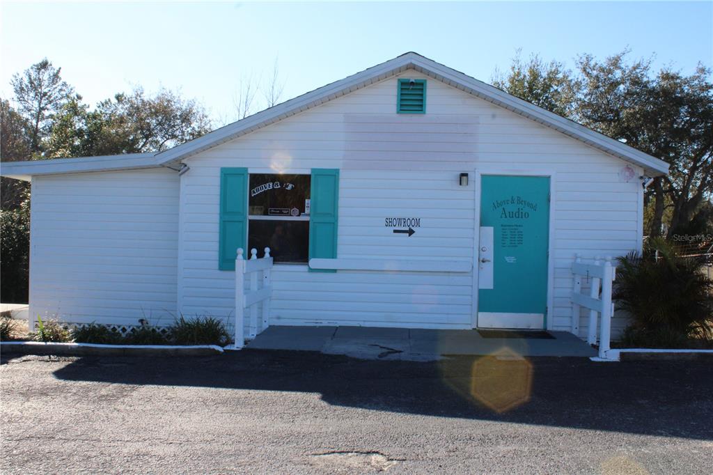 A white, single-story commercial building features a teal door, matching shutters, and a showroom sign — 5134 PLYNA STREET, SPRING HILL, FL