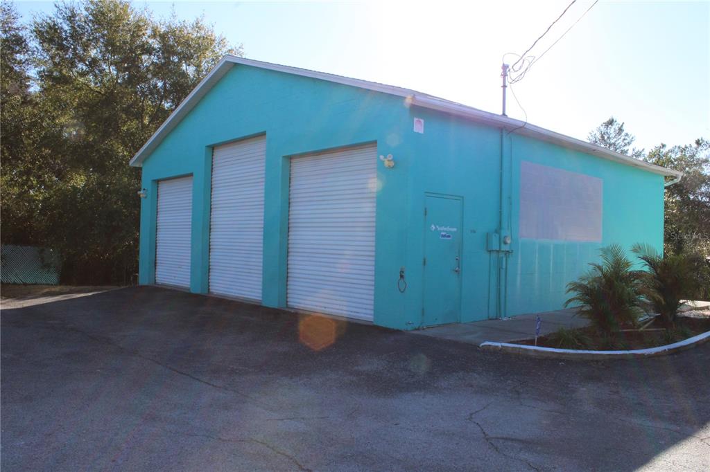 A bright teal commercial building features three roll-up garage doors and a single entry door — 5134 PLYNA STREET, SPRING HILL, FL