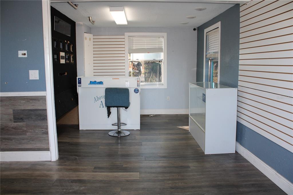 A commercial space features gray wood-look flooring, slat wall panels, a service counter, and a display case — 5134 PLYNA STREET, SPRING HILL, FL