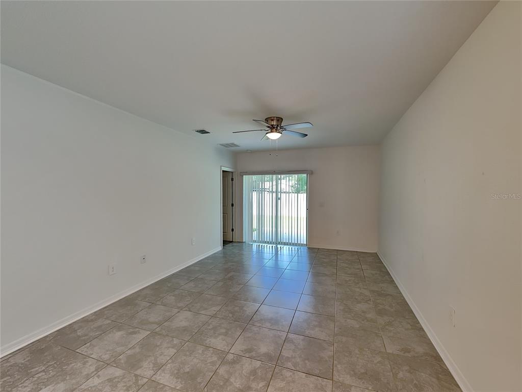 An empty room with light-colored tile flooring, a ceiling fan, and sliding glass doors — 4273 BABBLING BROOK WAY, KISSIMMEE, FL