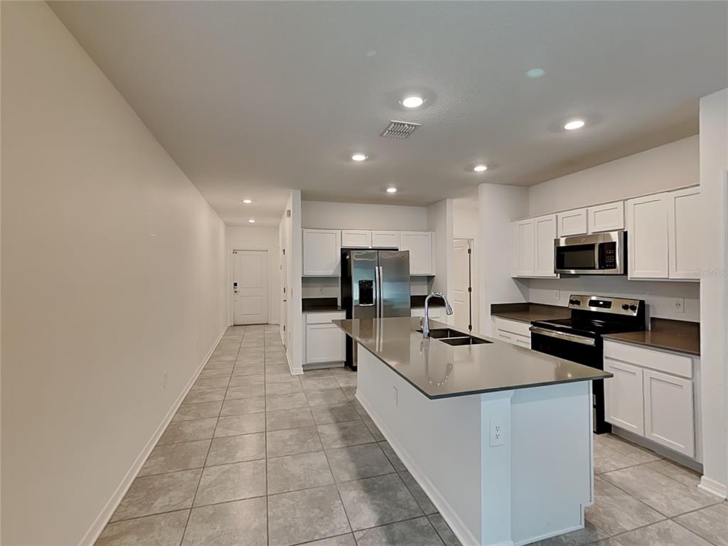 A modern kitchen features white cabinets, stainless steel appliances, and a large gray island — 4273 BABBLING BROOK WAY, KISSIMMEE, FL