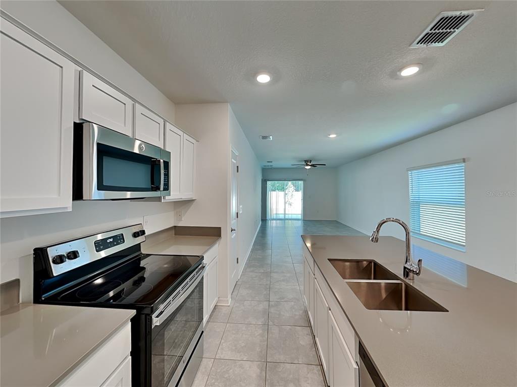 A kitchen with white cabinets, stainless steel appliances, and a central island with a sink — 4273 BABBLING BROOK WAY, KISSIMMEE, FL