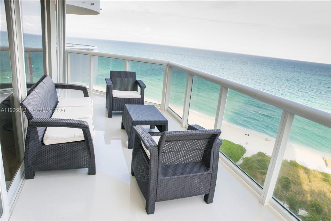 A balcony with wicker furniture overlooks the ocean and a sandy beach — 6301 Collins Ave # 1402, Miami Beach FL 33141, MIAMI BEACH, FL