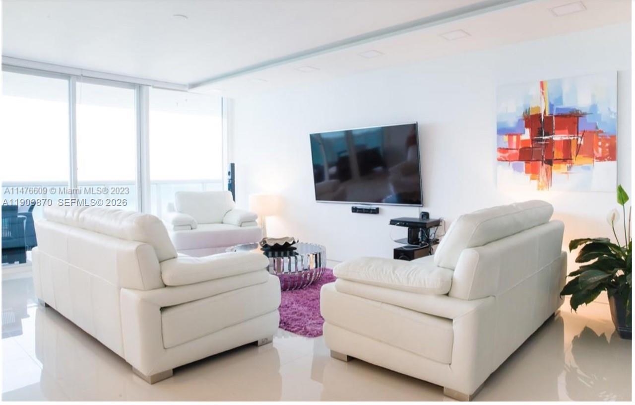 A bright living room features white leather sofas, a purple rug, and a wall-mounted television — 6301 Collins Ave # 1402, Miami Beach FL 33141, MIAMI BEACH, FL
