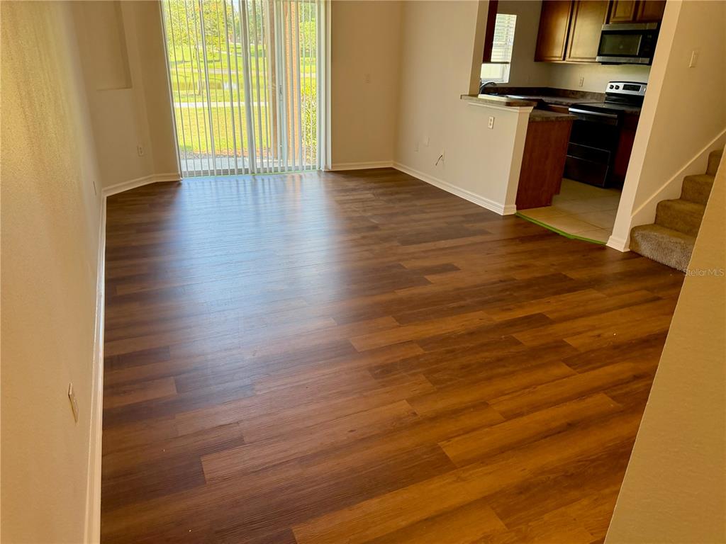 A living room with wood-look flooring, a sliding glass door, and an adjacent kitchen area — 1131 LONG OAK WAY, SANFORD, FL