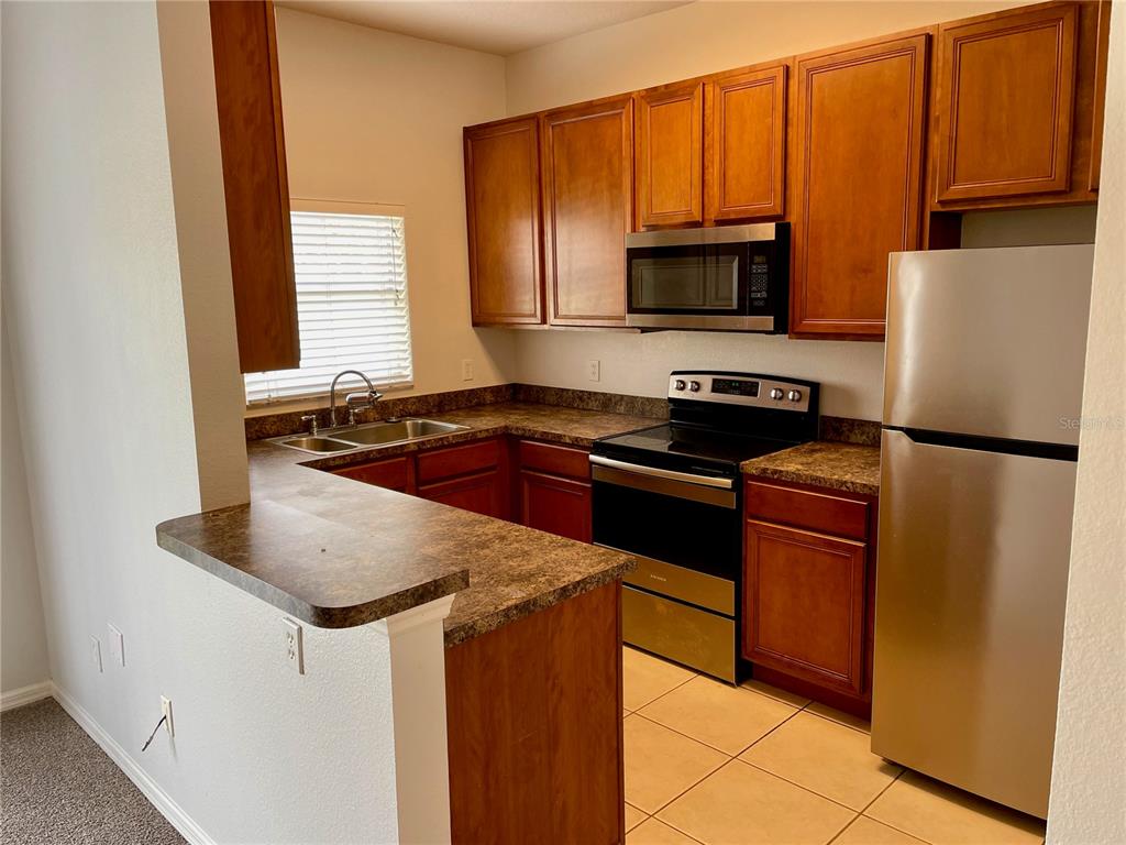 A kitchen features wooden cabinets, stainless steel appliances, and a breakfast bar with laminate countertops — 1131 LONG OAK WAY, SANFORD, FL