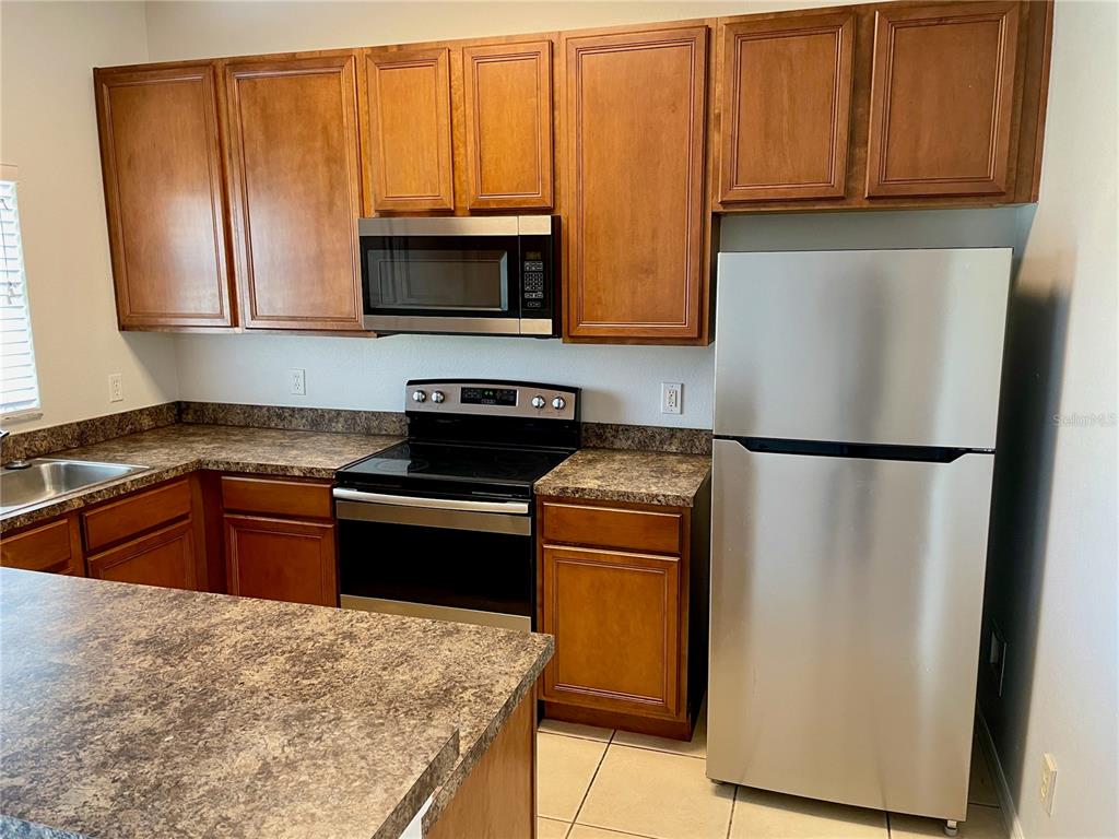 A kitchen features wood cabinets, a stainless steel microwave and refrigerator, and laminate countertops — 1131 LONG OAK WAY, SANFORD, FL
