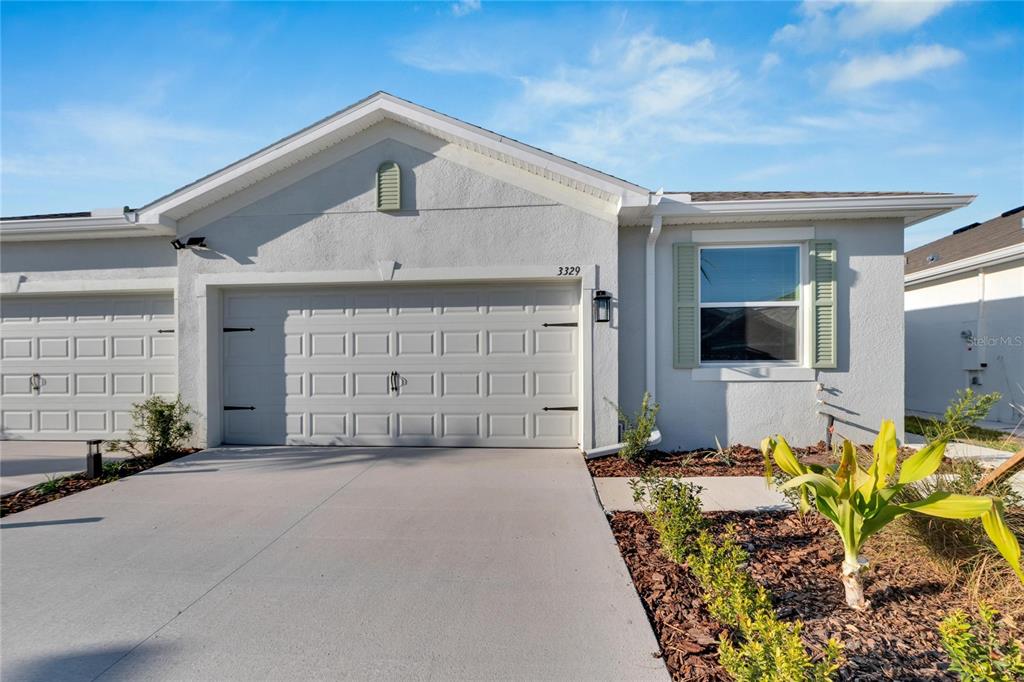 A light-colored house exterior features a two-car garage, a single window with shutters, and landscaping — 3329 SHADY SUNRISE LOOP, PLANT CITY, FL