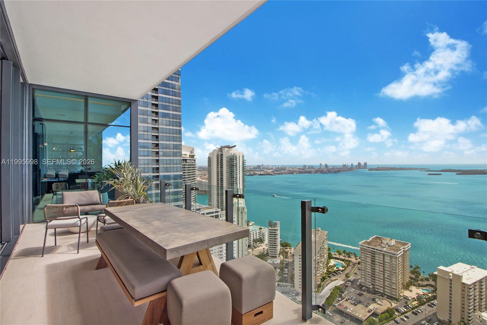 A high-rise balcony features a dining set overlooking a city skyline and the ocean — 1451 Brickell Ave # 4301, Miami FL 33131, MIAMI, FL