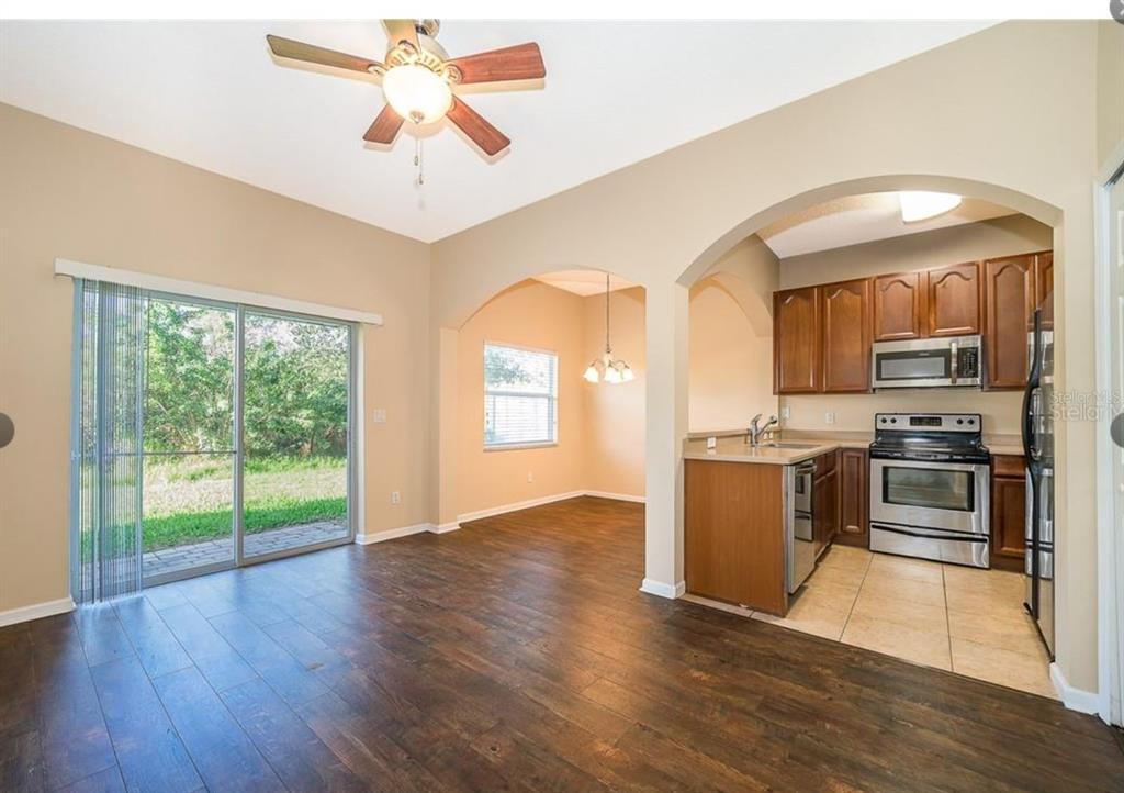 An open-concept living area with wood floors, a ceiling fan, and an adjacent tiled kitchen — 16432 CEDAR CREST DRIVE, ORLANDO, FL