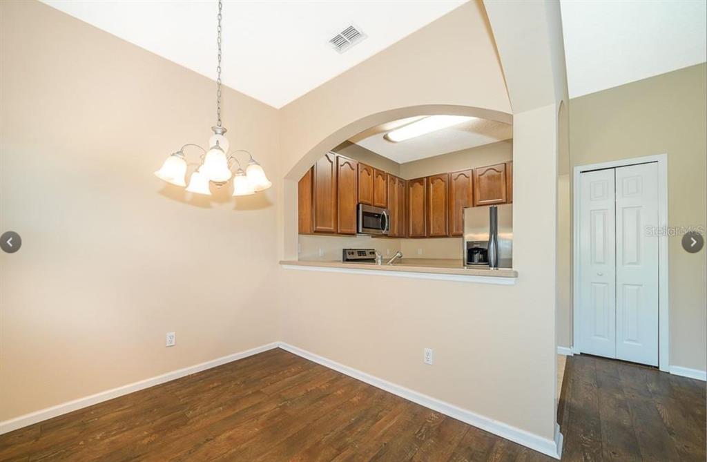 A dining area with a chandelier and wood floors opens into a kitchen with cabinets — 16432 CEDAR CREST DRIVE, ORLANDO, FL