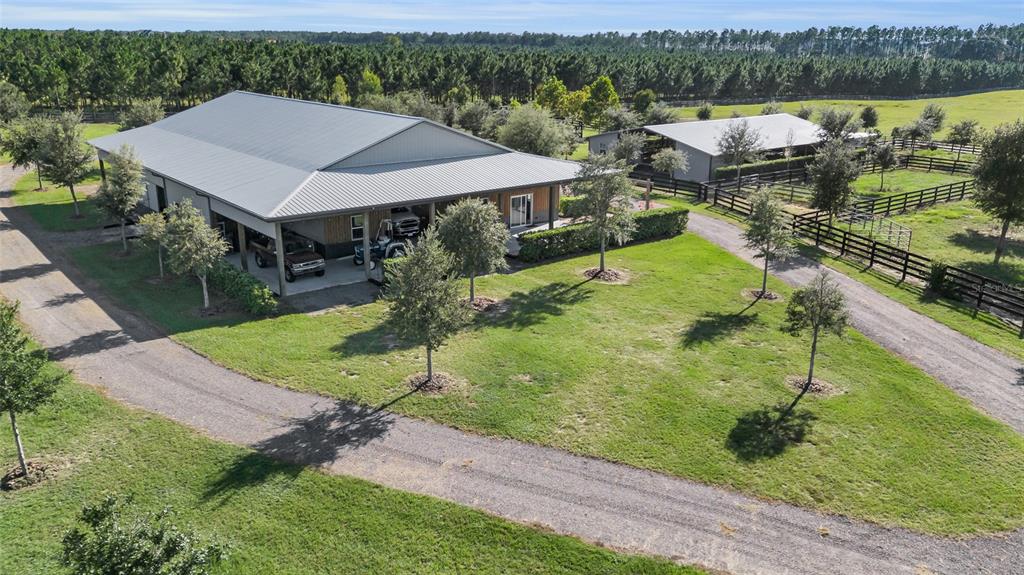 An aerial view shows a large metal building with a garage, adjacent barn, and fenced pastures — 9722 NW 26TH STREET, WILDWOOD, FL