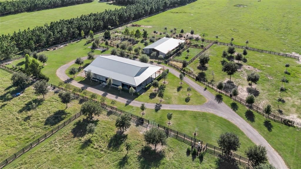 An aerial view shows a large metal-roofed barn, a round pen, and fenced pastures — 9722 NW 26TH STREET, WILDWOOD, FL