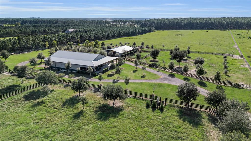 An aerial view shows a barn with a metal roof and a fenced dirt driveway — 9722 NW 26TH STREET, WILDWOOD, FL
