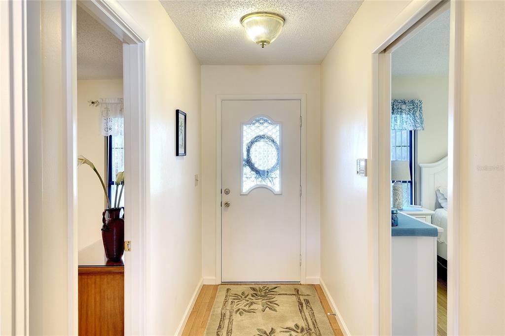 A hallway with a front door, light-colored walls, wood-look flooring, and a ceiling light fixture — 6004 VIVIENDA DRIVE UNIT 8, BRADENTON, FL
