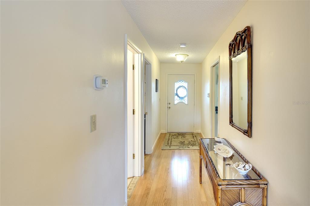 A hallway with hardwood floors, a console table, a mirror, and a front door — 6004 VIVIENDA DRIVE UNIT 8, BRADENTON, FL