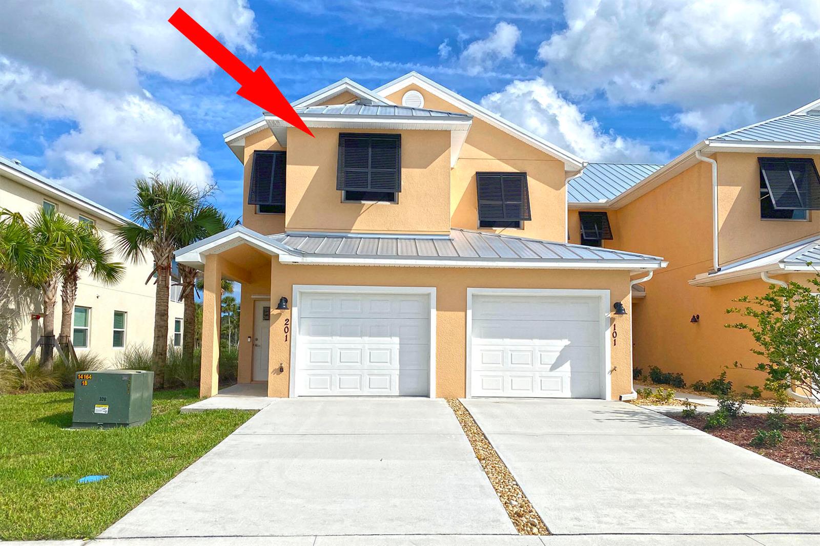 A two-story peach-colored townhome features a metal roof, white garage doors, and dark shutters — 3951 Playa Del Sol Drive # 201, Rockledge FL 32955, ROCKLEDGE, FL