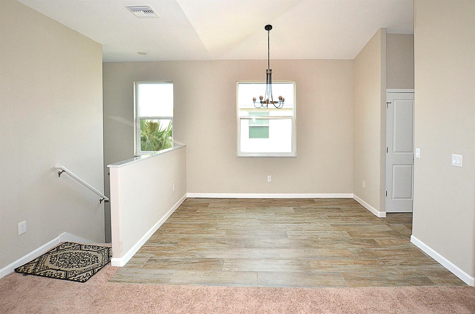 An empty dining area features wood-look tile flooring, a chandelier, and an adjacent staircase — 3951 Playa Del Sol Drive # 201, Rockledge FL 32955, ROCKLEDGE, FL