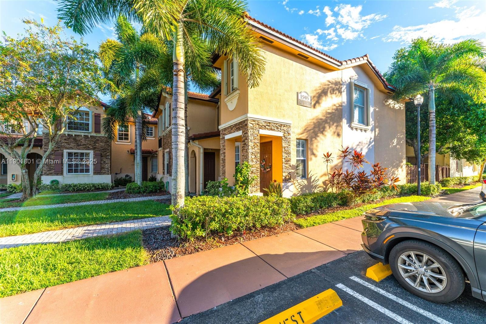 A two-story stucco townhouse with stone accents, palm trees, and a paved walkway — 1595 NE 33rd Rd # 3, Homestead FL 33033, HOMESTEAD, FL
