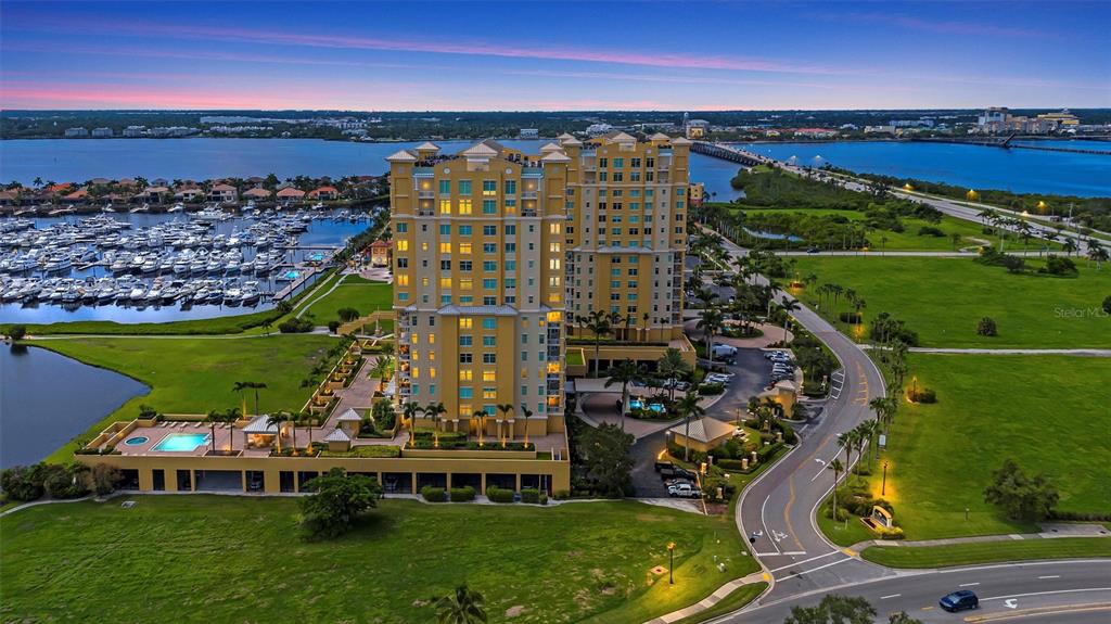 An aerial view shows a tall residential building with a pool and marina nearby — 140 RIVIERA DUNES WAY UNIT 206, PALMETTO, FL