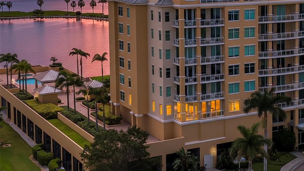 An aerial view of a multi-story apartment building with balconies overlooking a waterfront pool area — 140 RIVIERA DUNES WAY UNIT 206, PALMETTO, FL