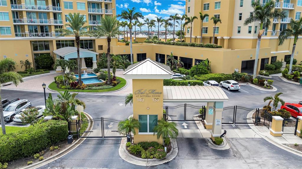 An aerial view shows the gated entrance and fountain of a multi-story residential complex — 140 RIVIERA DUNES WAY UNIT 206, PALMETTO, FL