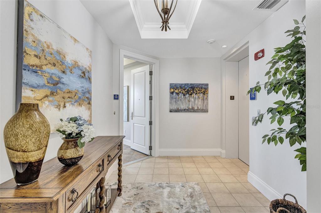 A tiled hallway features a wooden console table, two abstract paintings, and an elevator door — 140 RIVIERA DUNES WAY UNIT 206, PALMETTO, FL