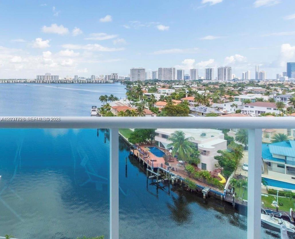 An elevated view from a balcony overlooking a canal, residential homes, and a distant skyline — 2841 NE 163rd St # 803, North Miami Beach FL 33160, NORTH MIAMI BEACH, FL