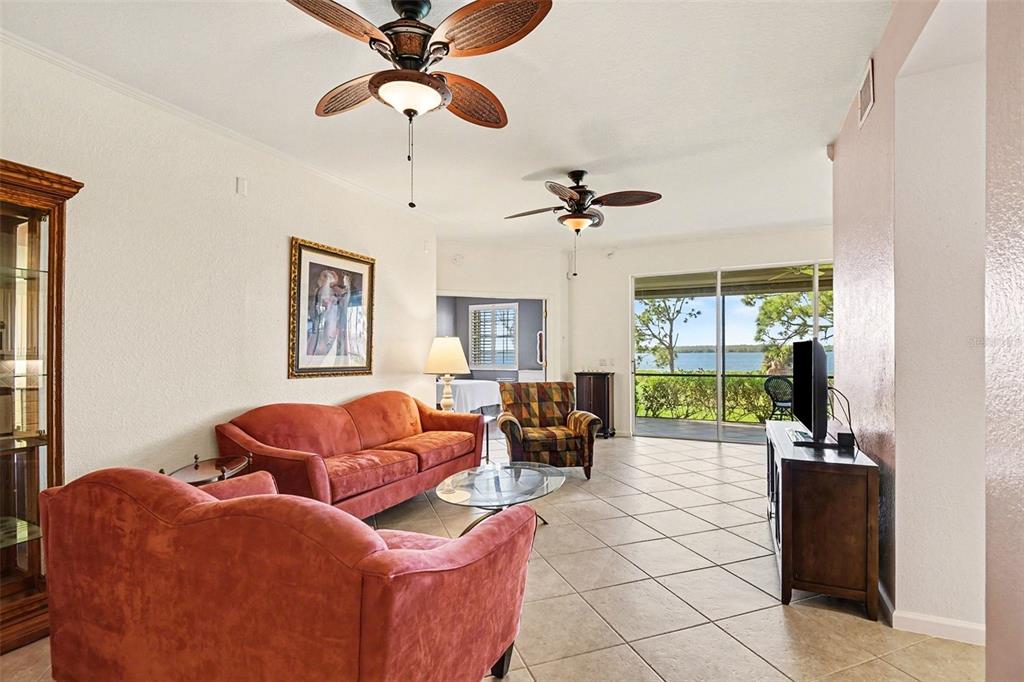 A living room features tile floors, two ceiling fans, and a view of the water — 4696 CLUB DRIVE UNIT 102, PORT CHARLOTTE, FL